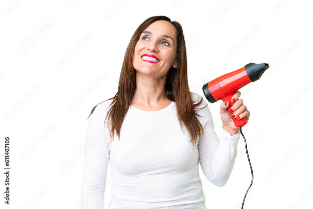 Middle age woman holding a hairdryer over isolated chroma key background looking up while smiling Middle age woman holding a hairdryer over isolated chroma key background looking up while smiling