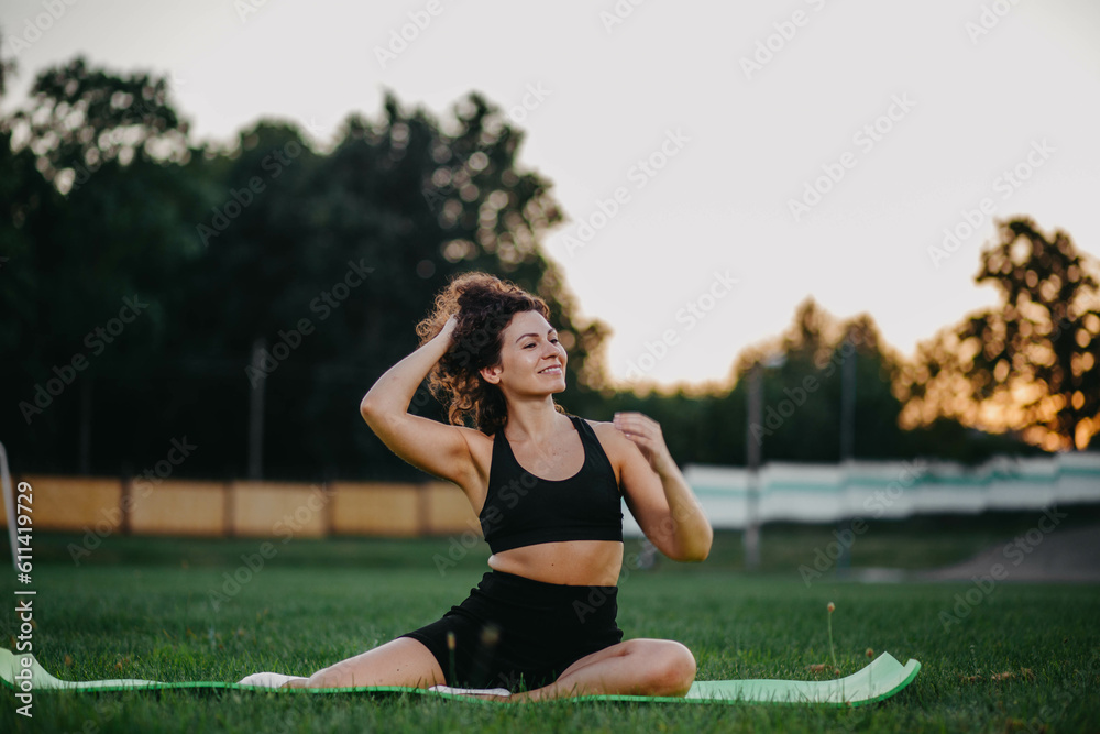 woman does yoga gymnastics on a gymnastic mat on the stadium grass in summer. Young mother in training woman does yoga gymnastics on a gymnastic mat on the stadium grass in summer. Young mother in training