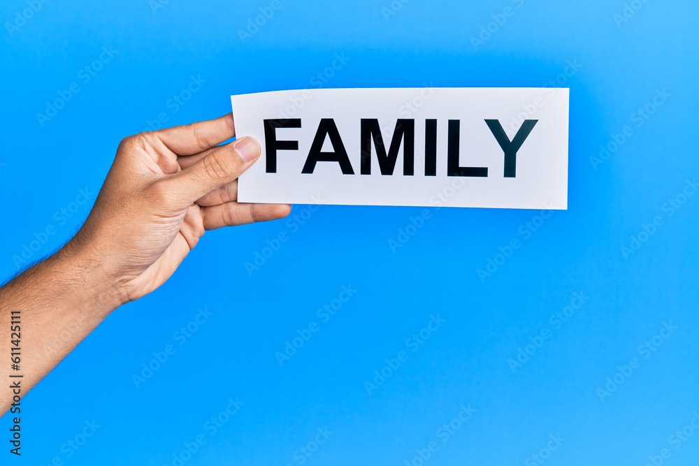 Hand of caucasian man holding paper with family word over isolated blue background Hand of caucasian man holding paper with family word over isolated blue background