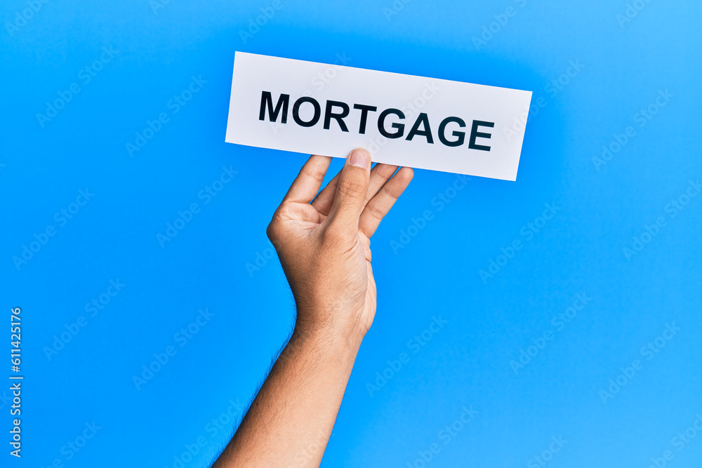 Hand of caucasian man holding paper with mortgage word over isolated blue background Hand of caucasian man holding paper with mortgage word over isolated blue background