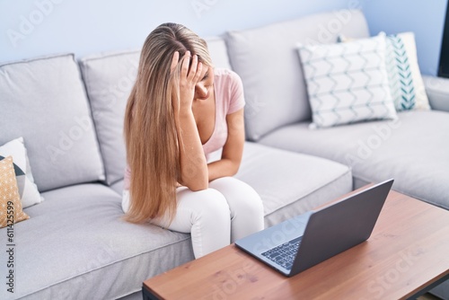 Young blonde woman using laptop with worried expression at home