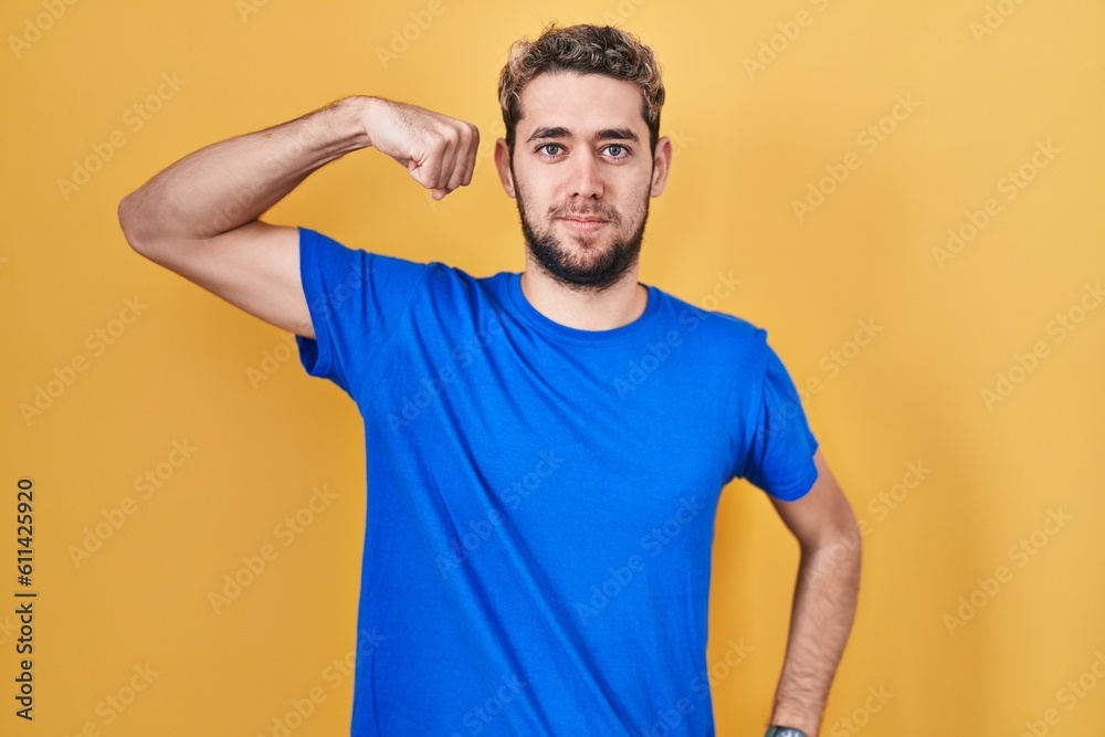 Hispanic man with beard standing over yellow background strong person showing arm muscle, confident and proud of power Hispanic man with beard standing over yellow background strong person showing arm muscle, confident and proud of power