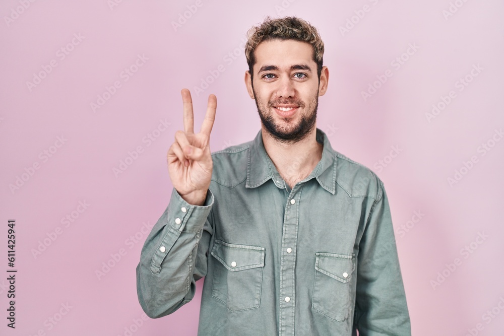 Hispanic man with beard standing over pink background showing and pointing up with fingers number two while smiling confident and happy. Hispanic man with beard standing over pink background showing and pointing up with fingers number two while smiling confident and happy.