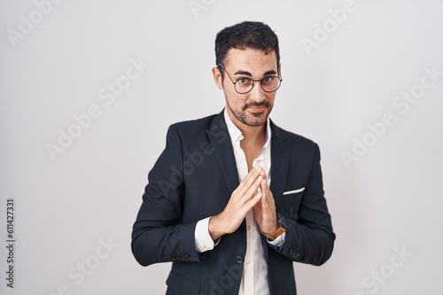 Handsome business hispanic man standing over white background hands together and fingers crossed smiling relaxed and cheerful. success and optimistic