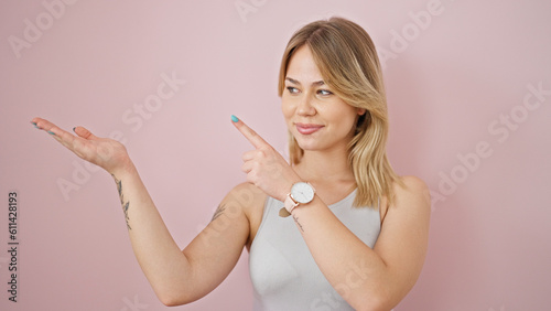 Young blonde woman smiling pointing to the side presenting over isolated pink background