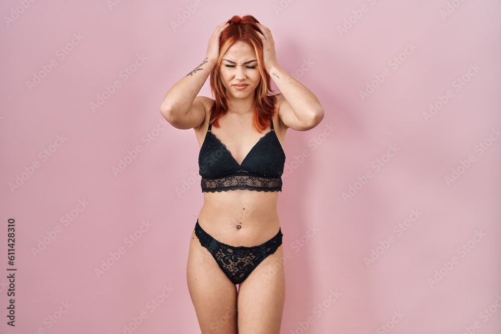 Obraz premium Young caucasian woman wearing lingerie over pink background suffering from headache desperate and stressed because pain and migraine. hands on head.