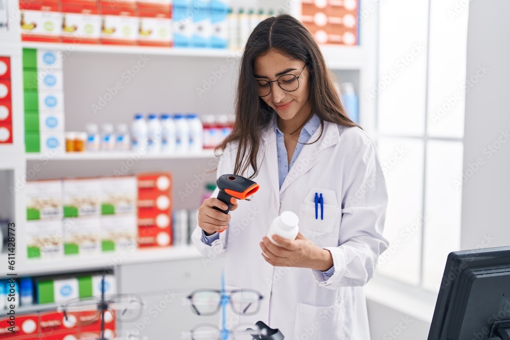 Young hispanic girl pharmacist scanning pills bottle at pharmacy