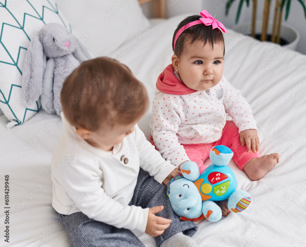 Adorable boy and girl sitting on bed playing with toys at bedroom Adorable boy and girl sitting on bed playing with toys at bedroom