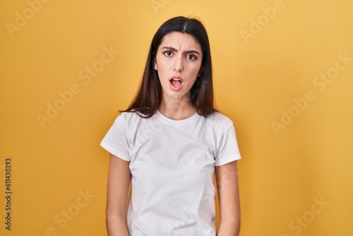 Obraz na plátně Young beautiful woman standing over yellow background in shock face, looking ske