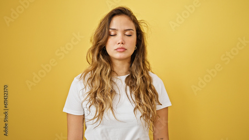 Young beautiful hispanic woman standing with serious expression and close eyes over isolated yellow background