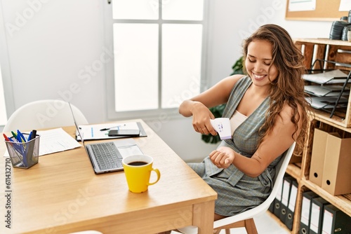 Young beautiful hispanic woman business worker measuring temperature at office