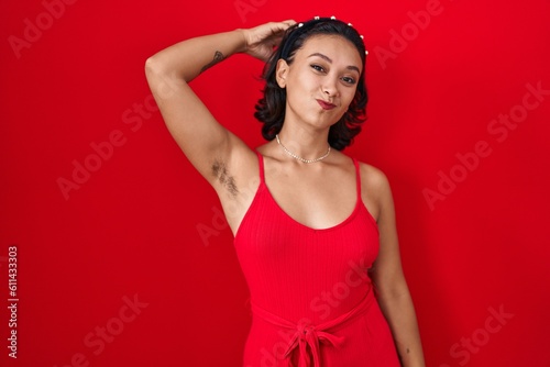 Young hispanic woman standing over red background confuse and wonder about question. uncertain with doubt, thinking with hand on head. pensive concept. © Krakenimages.com