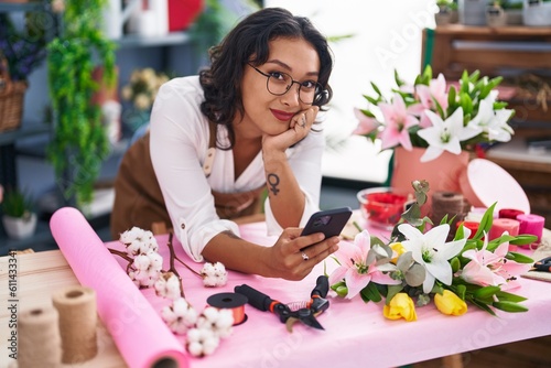 Young beautiful hispanic woman florist using smartphone leaning on table at flower shop