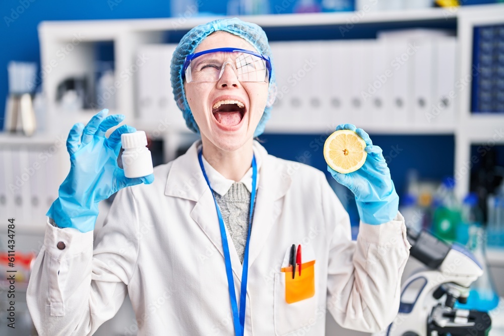 Beautiful woman working at scientist laboratory holding pills and lemon angry and mad screaming frustrated and furious, shouting with anger looking up. Beautiful woman working at scientist laboratory holding pills and lemon angry and mad screaming frustrated and furious, shouting with anger looking up.