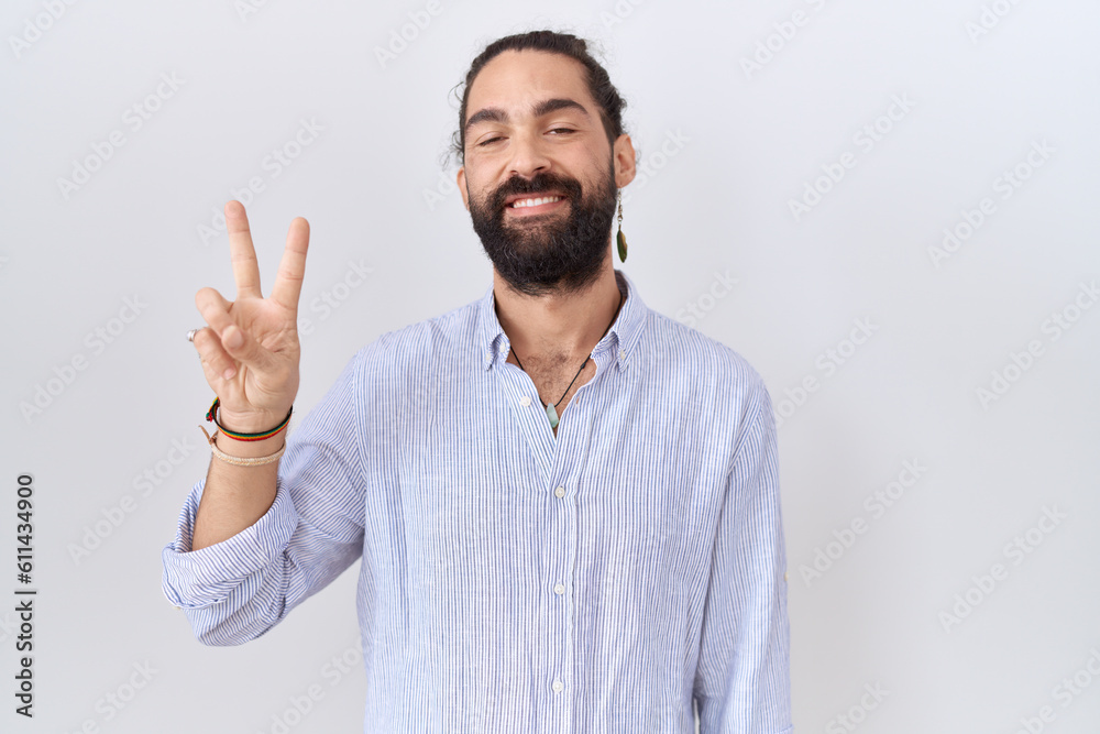Naklejka premium Hispanic man with beard wearing casual shirt showing and pointing up with fingers number two while smiling confident and happy.