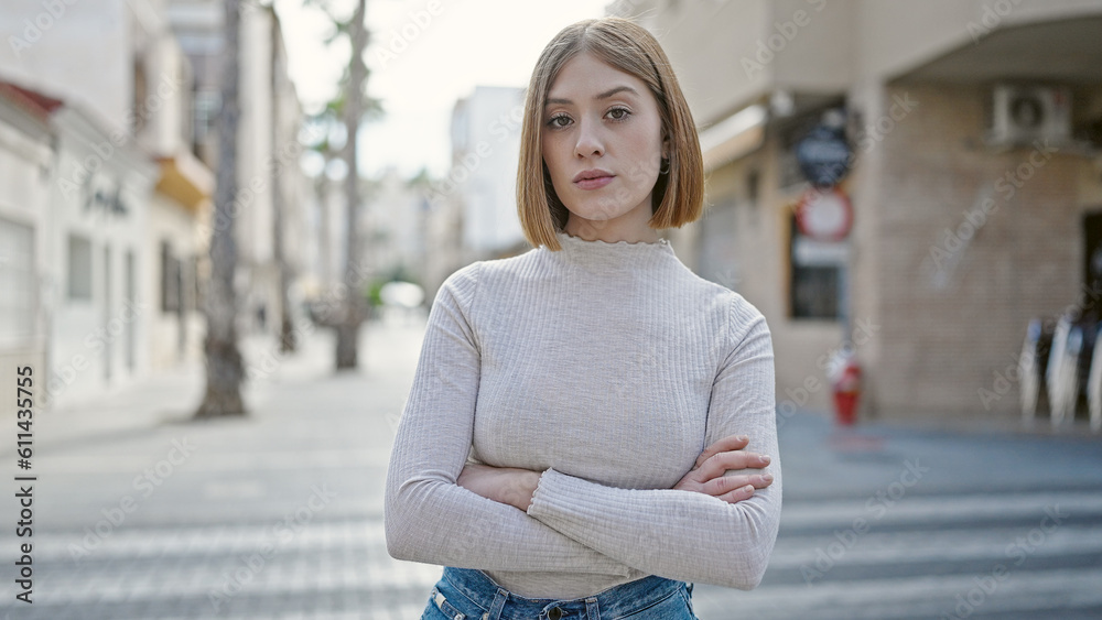 Young blonde woman standing with serious expression and arms crossed gesture at street Young blonde woman standing with serious expression and arms crossed gesture at street