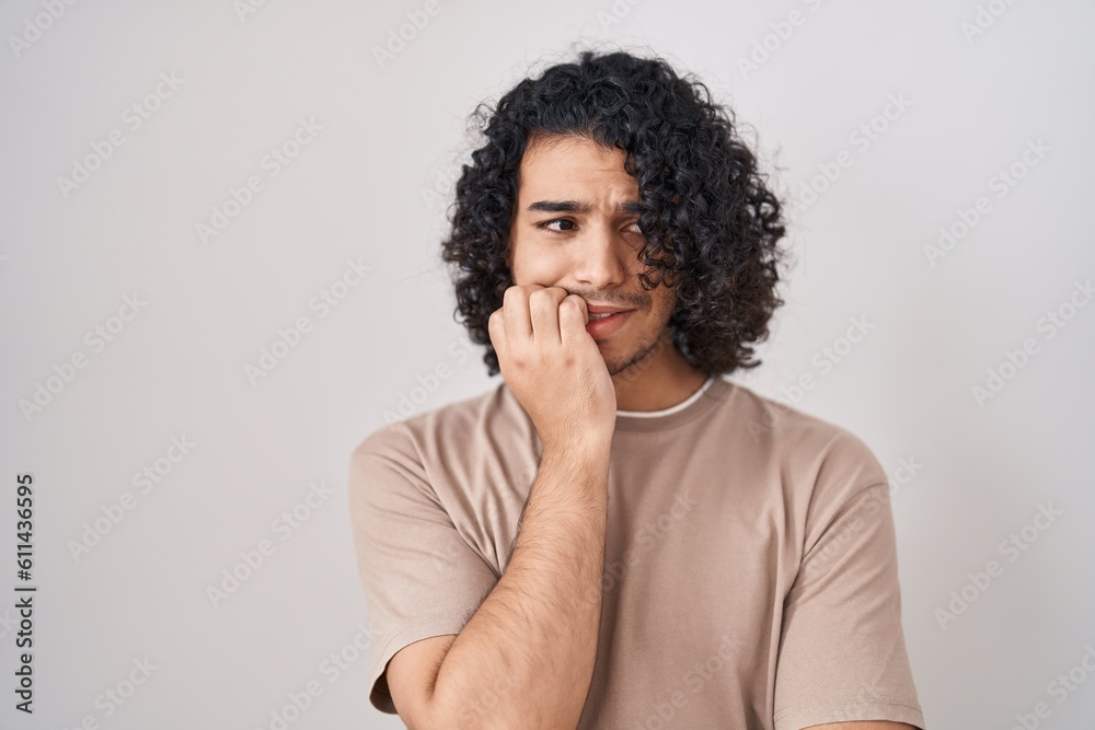 Hispanic man with curly hair standing over white background looking stressed and nervous with hands on mouth biting nails. anxiety problem. Hispanic man with curly hair standing over white background looking stressed and nervous with hands on mouth biting nails. anxiety problem.
