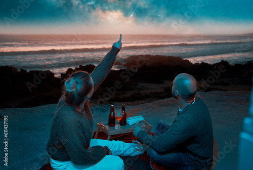 back view caucasian couple sitting in viewpoint having picnic and watching the starry sky over the ocean