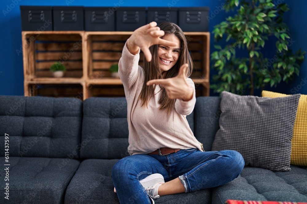 Beautiful woman sitting on the sofa at home smiling making frame with hands and fingers with happy face. creativity and photography concept. Beautiful woman sitting on the sofa at home smiling making frame with hands and fingers with happy face. creativity and photography concept.