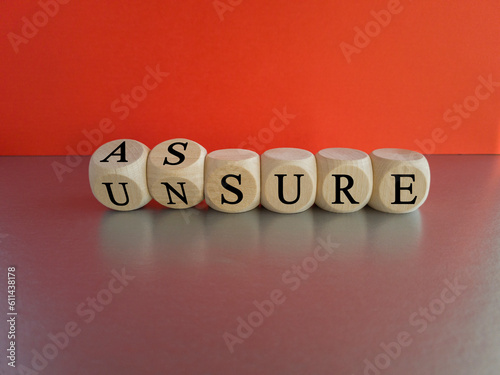 Assure or unsure symbol. Turned wooden cubes and changed the concept word unsure to assure. Beautiful grey table, red background, copy space. Business and assure or unsure concept. photo