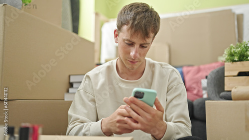 Young caucasian man using smartphone with relaxed expression at new home