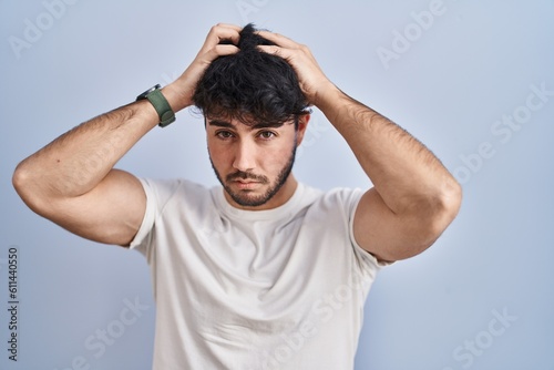 Hispanic man with beard standing over white background suffering from headache desperate and stressed because pain and migraine. hands on head.