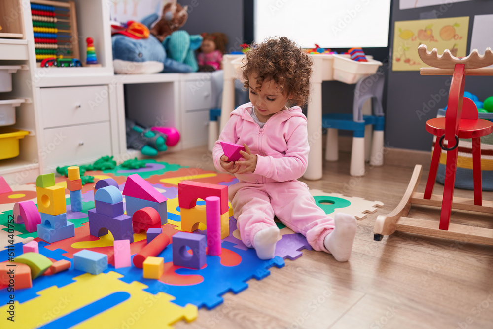 Fototapeta premium Adorable hispanic girl playing with construction blocks sitting on floor at kindergarten