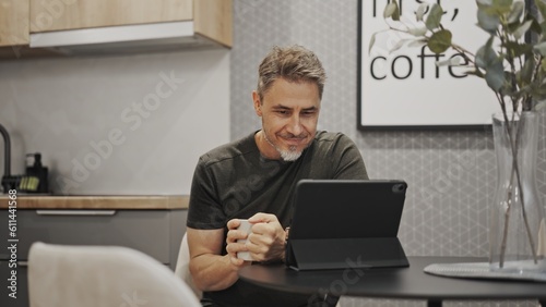 Man working with tablet computer in home office. Sitting at coffee table, drinking. Online in cafe.