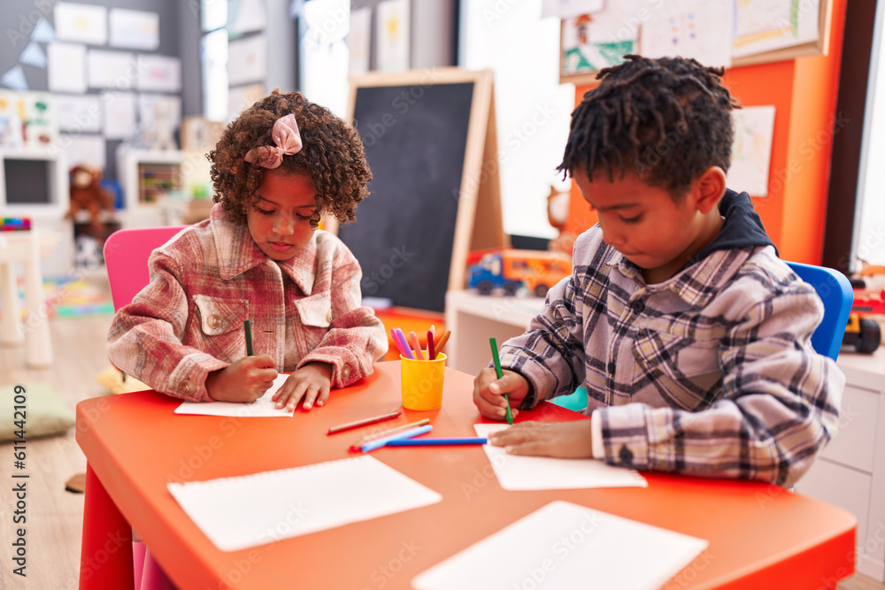 Adorable african american boy and girl preschool students sitting on table drawing on paper at kindergarten Adorable african american boy and girl preschool students sitting on table drawing on paper at kindergarten