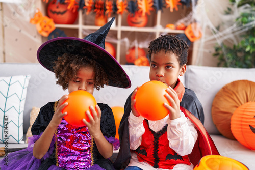 Adorable african american boy and girl having halloween party inflating balloon at home