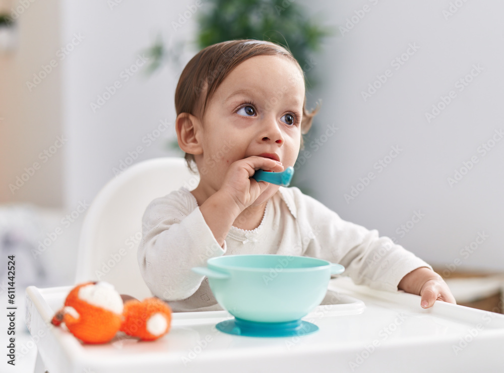 Adorable hispanic boy sitting on highchair sucking spoon at bedroom Adorable hispanic boy sitting on highchair sucking spoon at bedroom