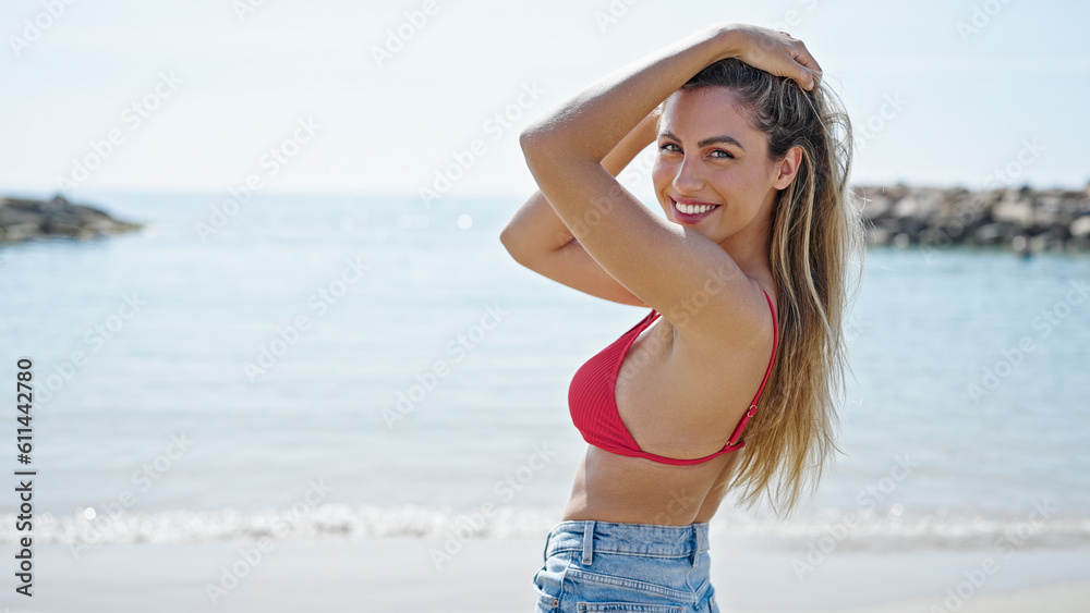Young blonde woman tourist wearing bikini combing hair with hands at beach Young blonde woman tourist wearing bikini combing hair with hands at beach