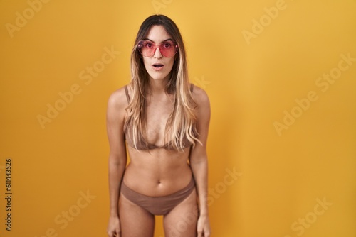 Young hispanic woman wearing bikini over yellow background afraid and shocked with surprise and amazed expression, fear and excited face.