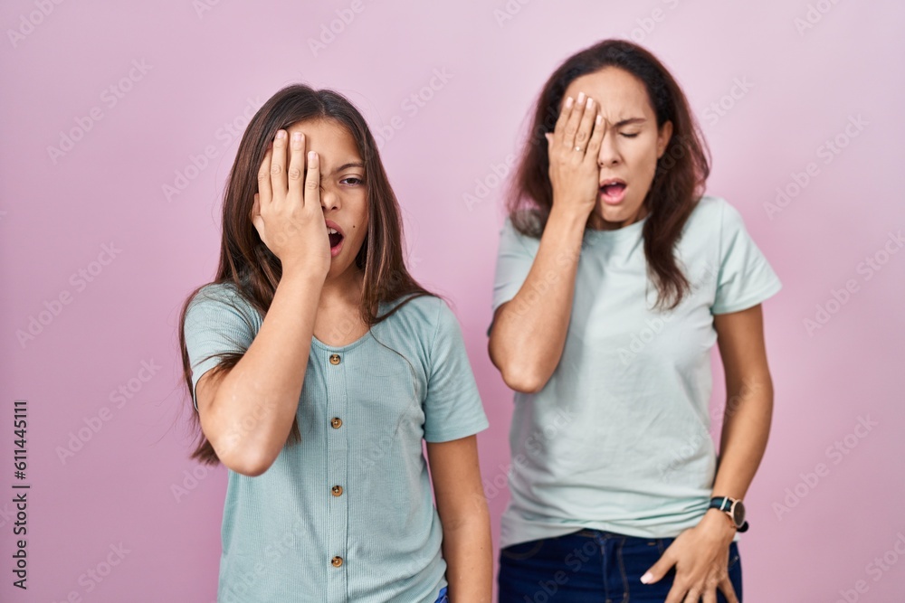 Young mother and daughter standing over pink background yawning tired covering half face, eye and mouth with hand. face hurts in pain. Young mother and daughter standing over pink background yawning tired covering half face, eye and mouth with hand. face hurts in pain.