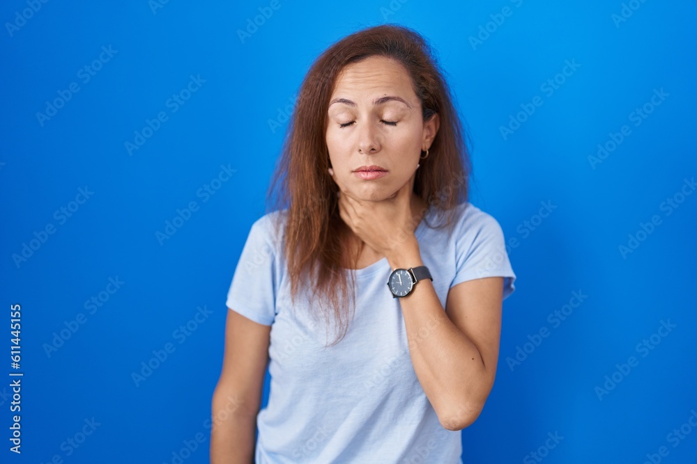Brunette woman standing over blue background touching painful neck, sore throat for flu, clod and infection Brunette woman standing over blue background touching painful neck, sore throat for flu, clod and infection