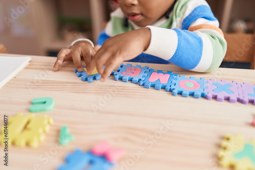 African american boy playing with vocabulary puzzle game sitting on table at kindergarten