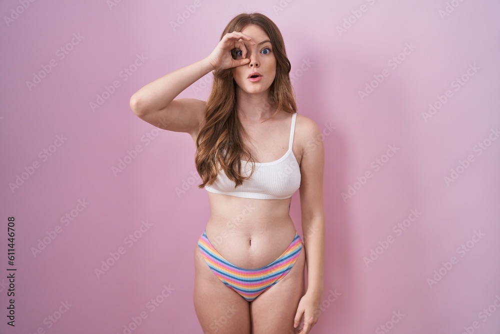 Naklejka premium Caucasian woman wearing lingerie over pink background doing ok gesture shocked with surprised face, eye looking through fingers. unbelieving expression.