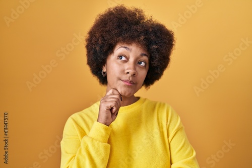 Young african american woman standing over yellow background with hand on chin thinking about question, pensive expression. smiling with thoughtful face. doubt concept. © Krakenimages.com