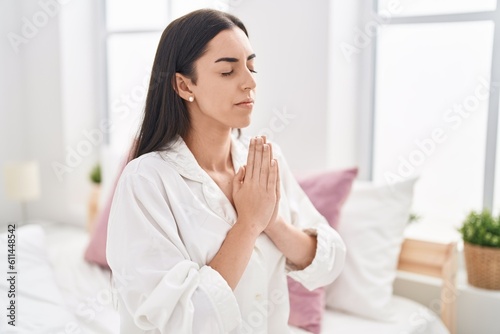Young hispanic woman praying sitting on bed at bedroom © Krakenimages.com