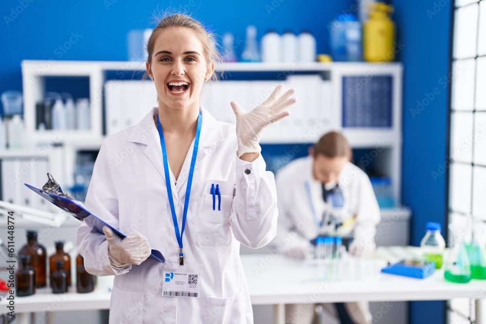 Blonde woman working at scientist laboratory celebrating victory with happy smile and winner expression with raised hands