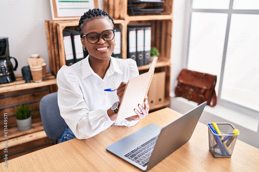 African american woman business worker using laptop writing on notebook at office African american woman business worker using laptop writing on notebook at office
