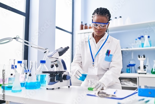 African american woman scientist smiling confident pouring liquid on test tube at laboratory