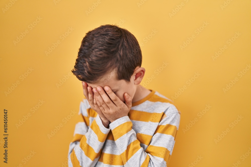 Young caucasian kid standing over yellow background with sad expression covering face with hands while crying. depression concept. Young caucasian kid standing over yellow background with sad expression covering face with hands while crying. depression concept.