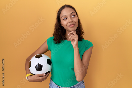 Young hispanic woman holding ball with hand on chin thinking about question, pensive expression. smiling and thoughtful face. doubt concept. © Krakenimages.com