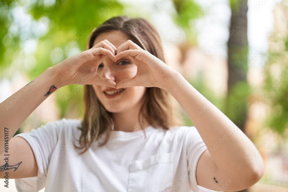 Young woman smiling confident doing heart gesture with hands at park