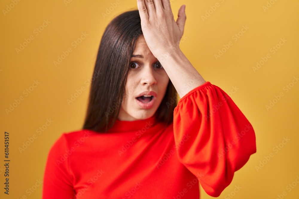 Young hispanic woman standing over yellow background surprised with hand on head for mistake, remember error. forgot, bad memory concept. Young hispanic woman standing over yellow background surprised with hand on head for mistake, remember error. forgot, bad memory concept.