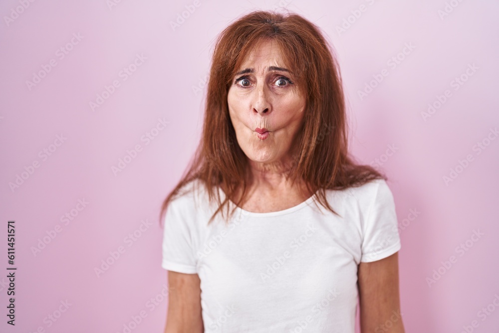 Middle age woman standing over pink background making fish face with lips, crazy and comical gesture. funny expression. Middle age woman standing over pink background making fish face with lips, crazy and comical gesture. funny expression.