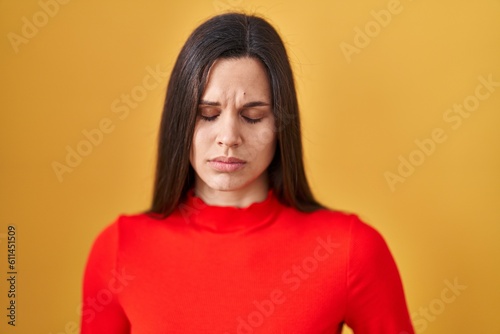 Young hispanic woman standing over yellow background with hand on stomach because indigestion, painful illness feeling unwell. ache concept.