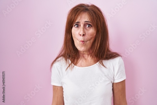 Middle age woman standing over pink background making fish face with lips, crazy and comical gesture. funny expression.