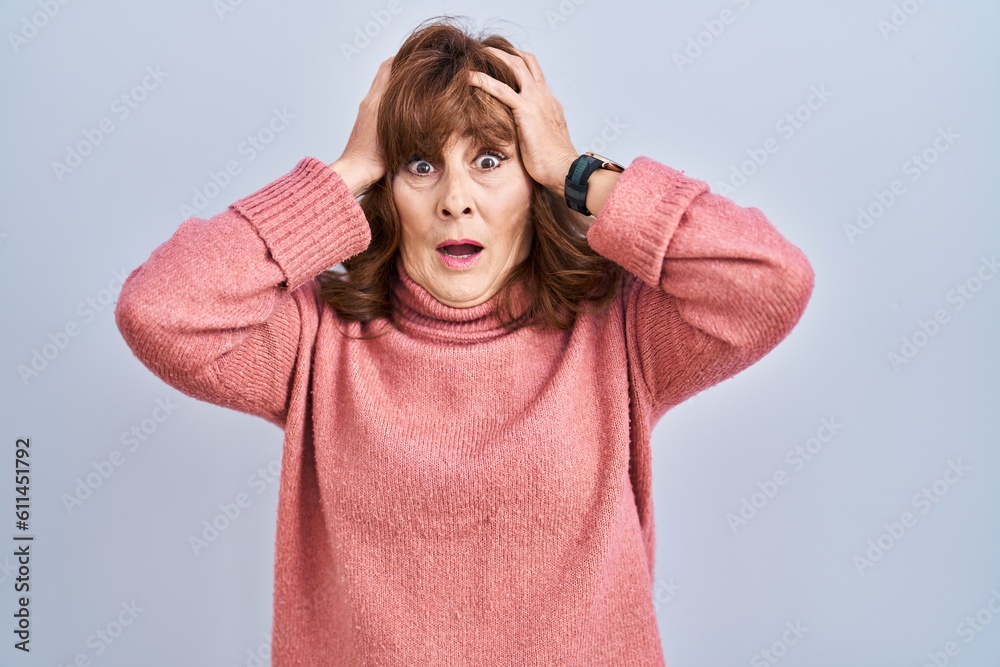Middle age hispanic woman standing over isolated background crazy and scared with hands on head, afraid and surprised of shock with open mouth Middle age hispanic woman standing over isolated background crazy and scared with hands on head, afraid and surprised of shock with open mouth